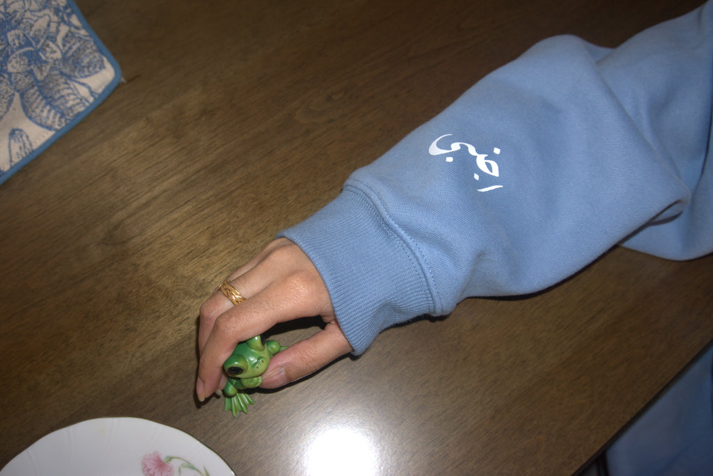 Hand holding a small green toy on a wooden surface with a blue sleeve and text overlay.